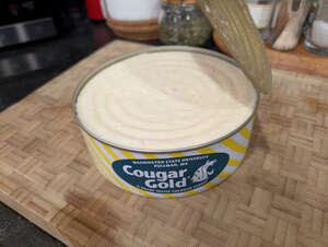 An opened tin can of Cougar Gold cheese from Washington State University resting on wooden cutting board.